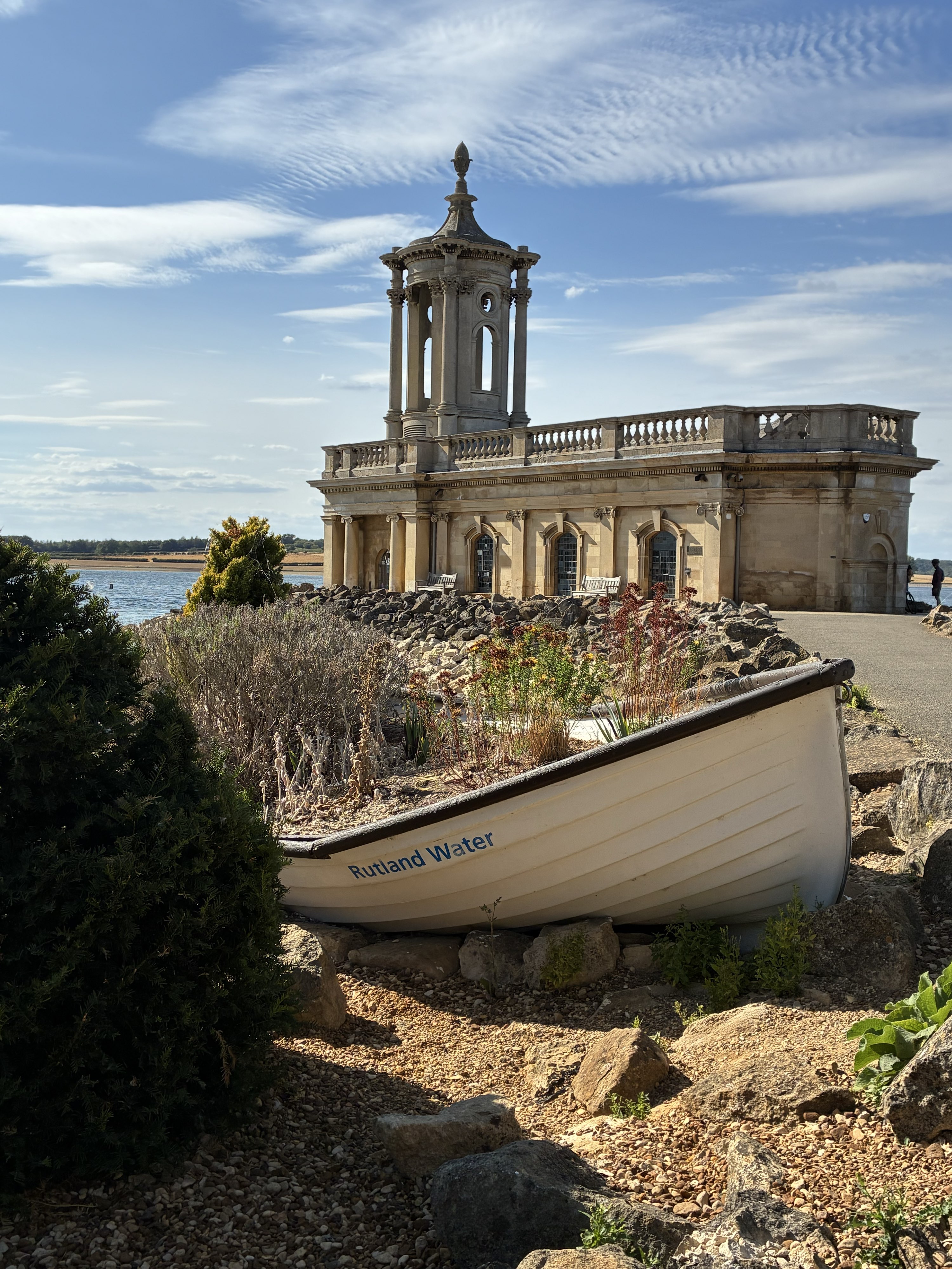 Normanton Church with a rowing boat in the foreground and an ornamental garden.